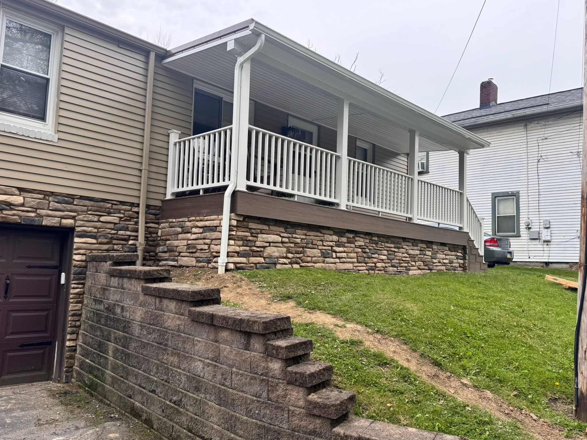 House with front porch, stone retaining wall, concrete steps, and sloped grassy yard