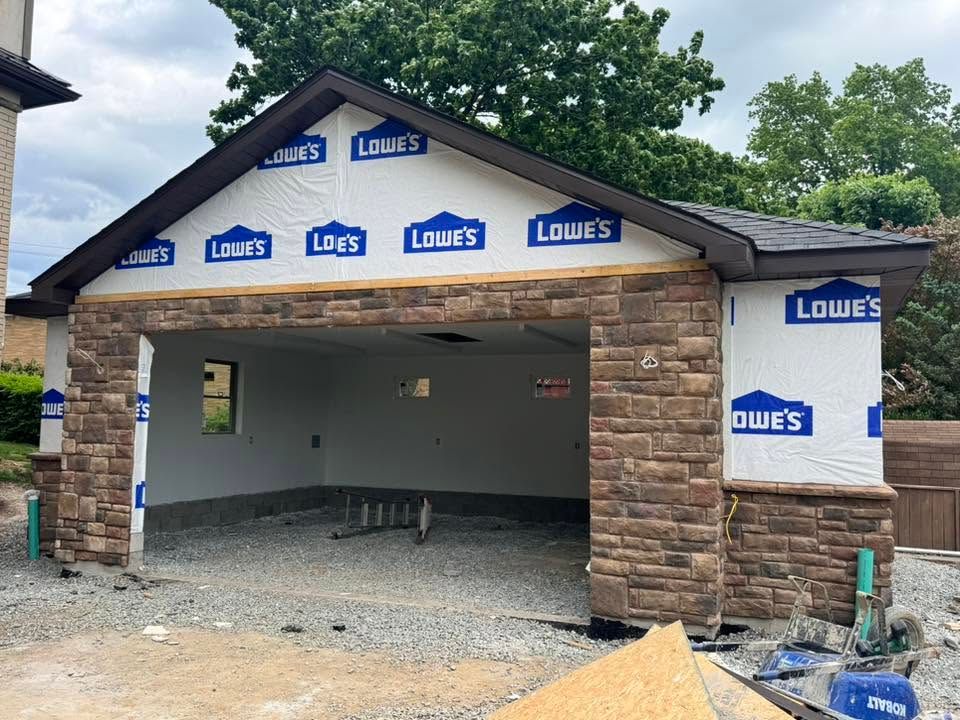 Partially built garage with blue Lowe's house wrap and exposed gravel floor