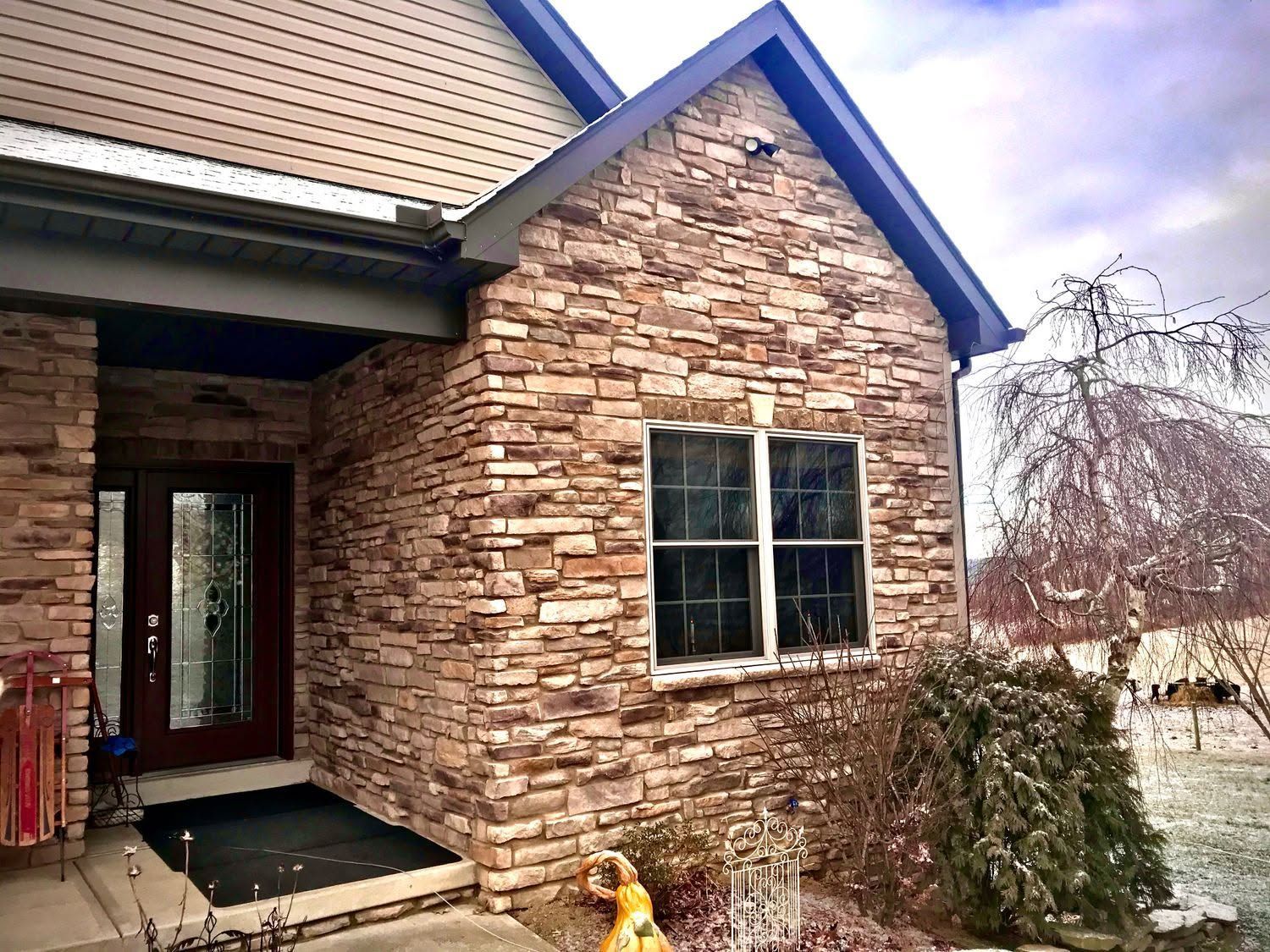 Stone house exterior with front porch, window, and snowy yard