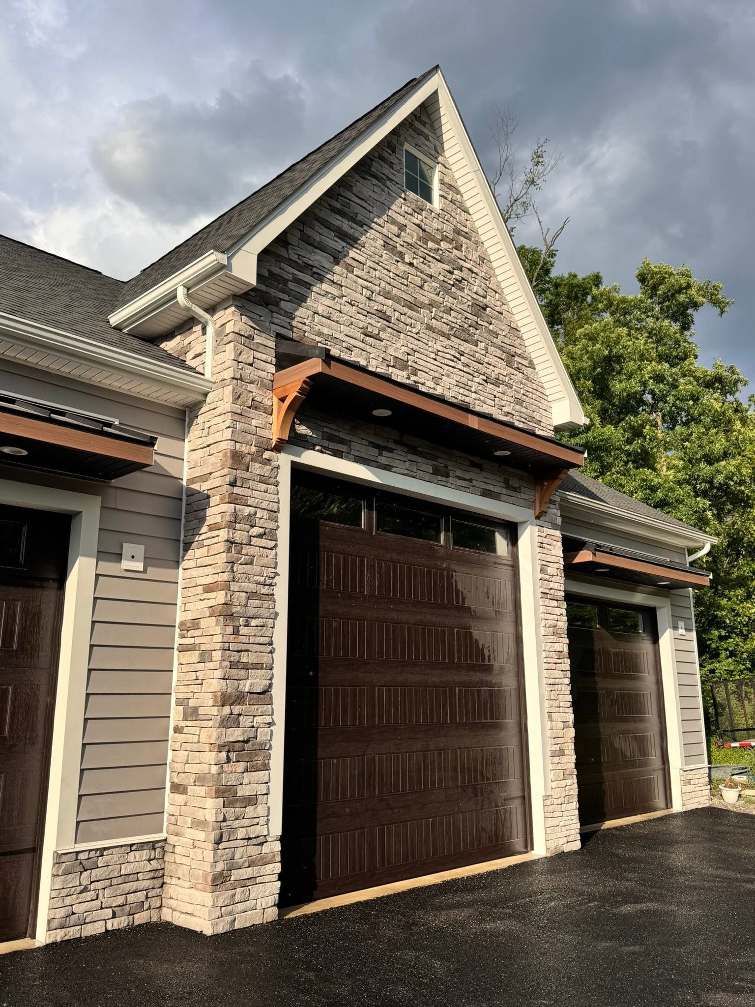 Stone-trimmed garage with dark wooden door and steep gabled roof under cloudy sky