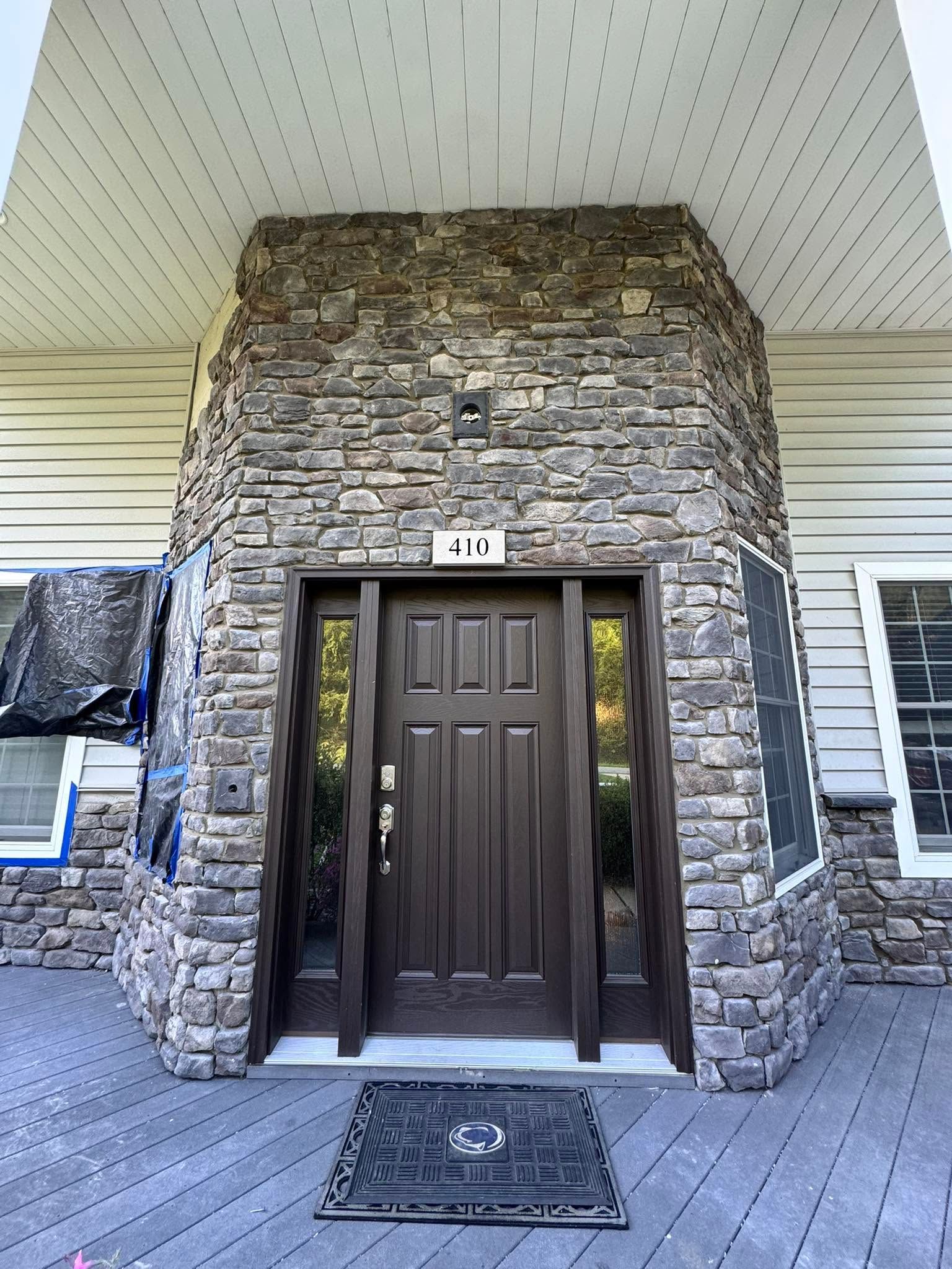 Stone apartment entryway with dark brown front door under a covered porch, framed by white siding and gray flooring