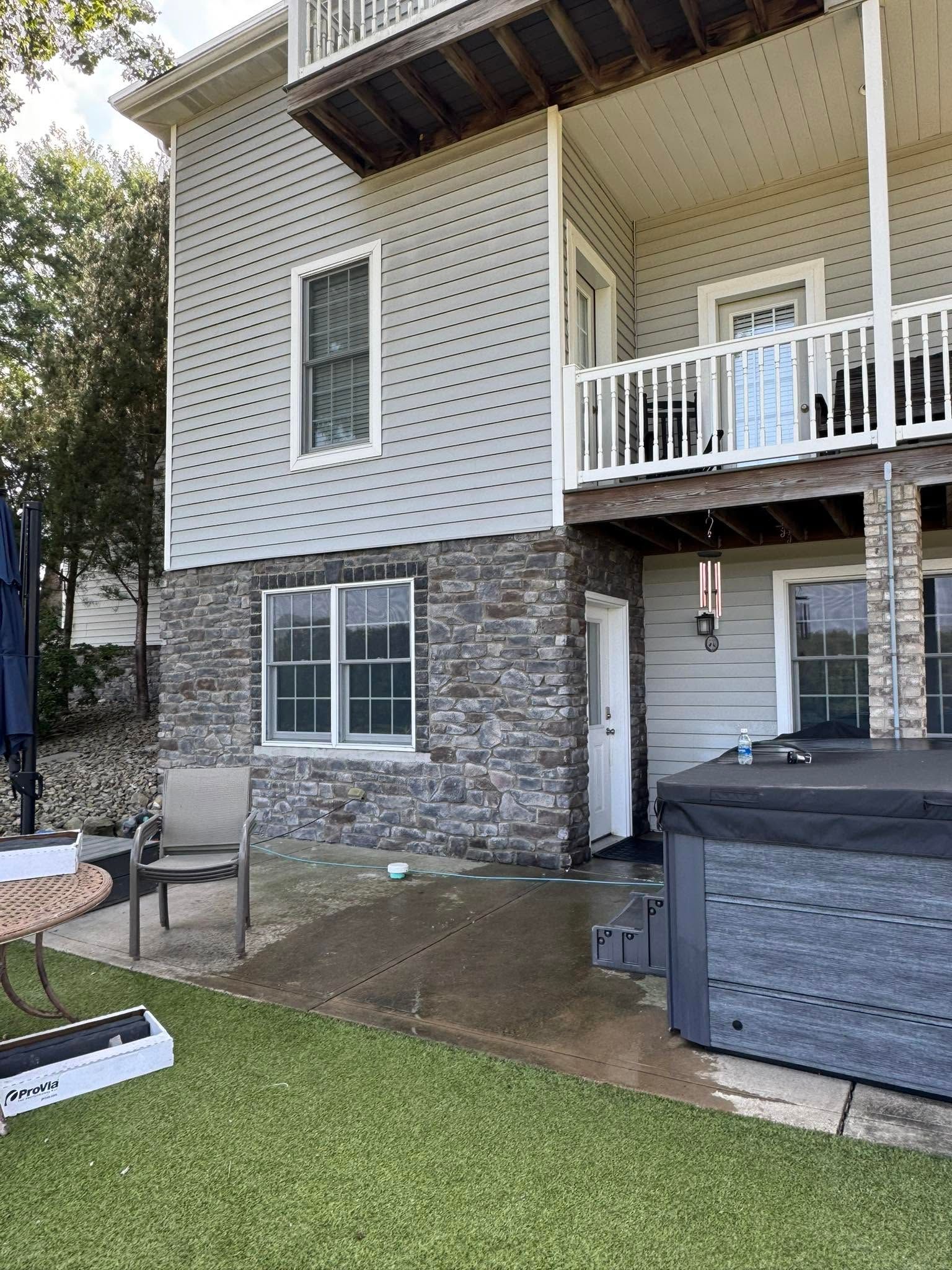 Backyard patio with stone and white siding house, sliding glass door, balcony, and gray hot tub cover