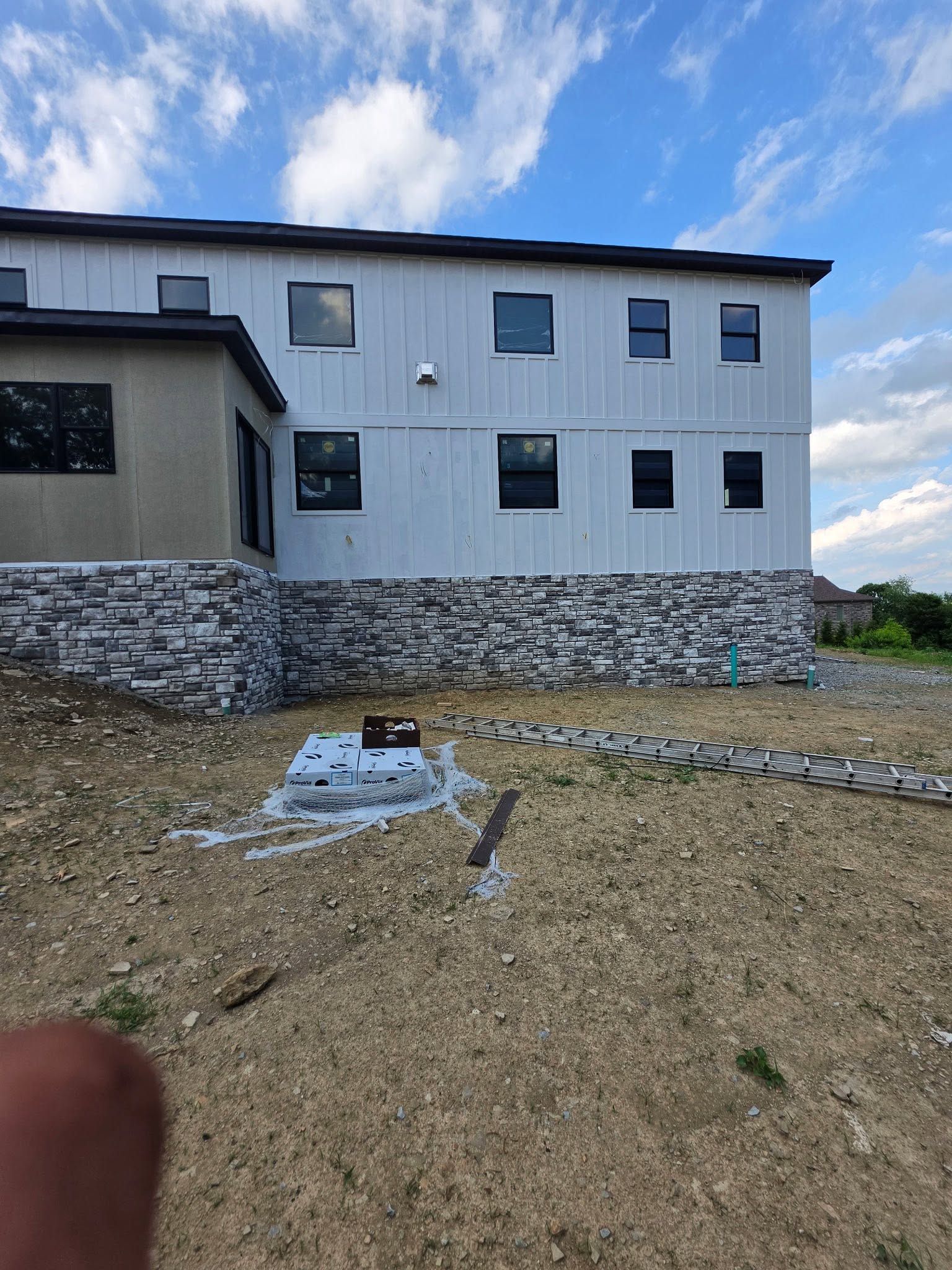 Two-story white house on a rocky lot under a partly cloudy sky, with a bare dirt foreground.