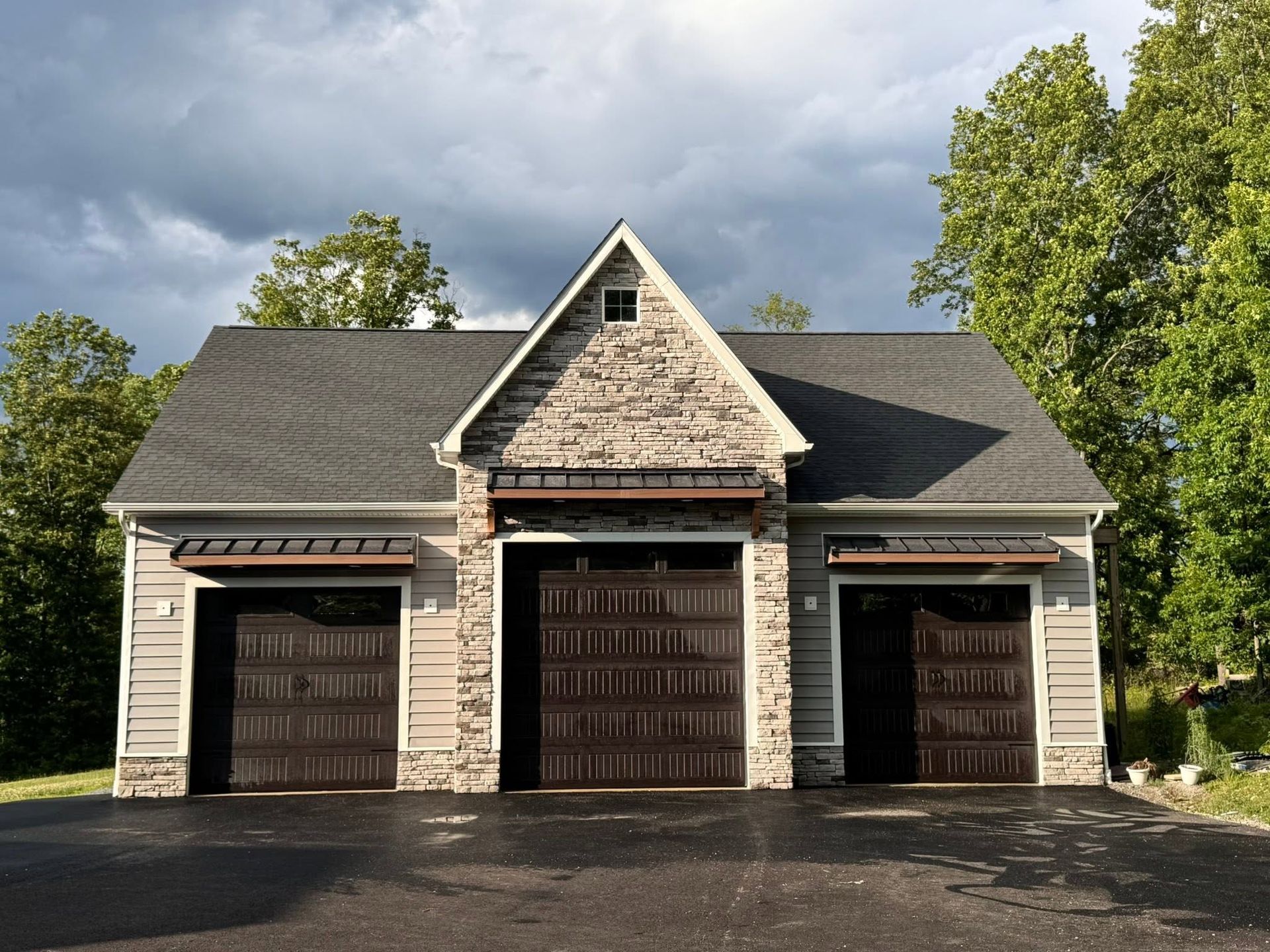 Three-car garage with stone center and dark doors under a cloudy sky
