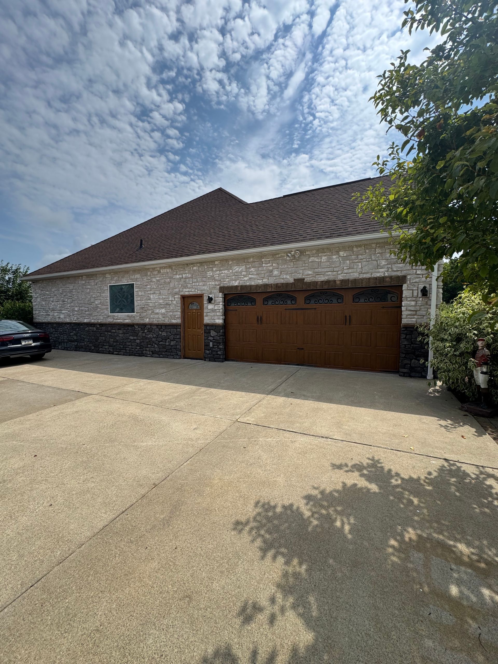 Brick house with brown garage doors and gravel driveway under a partly cloudy sky