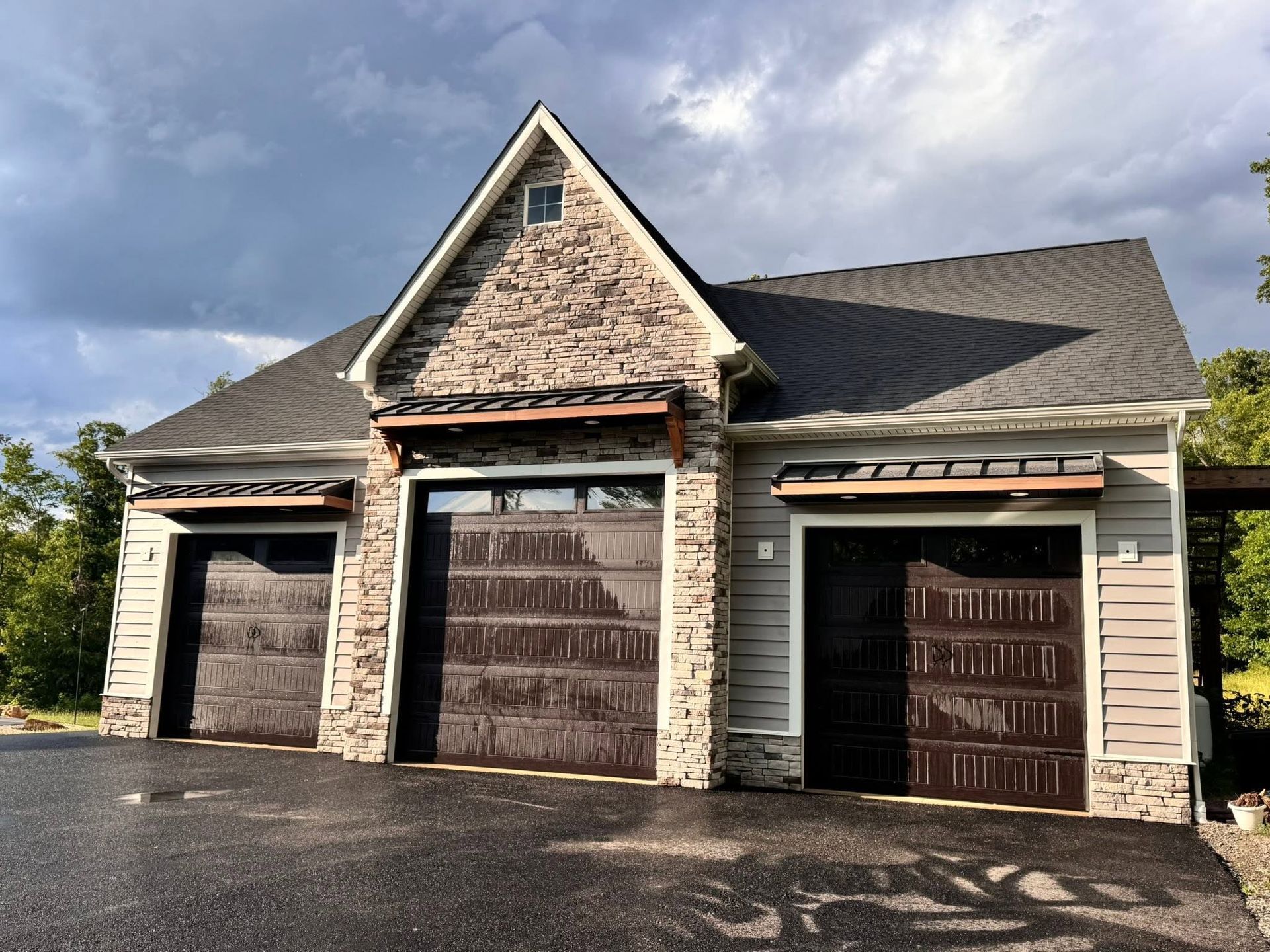 Three-car garage exterior with stone gable and brown doors on a clear day