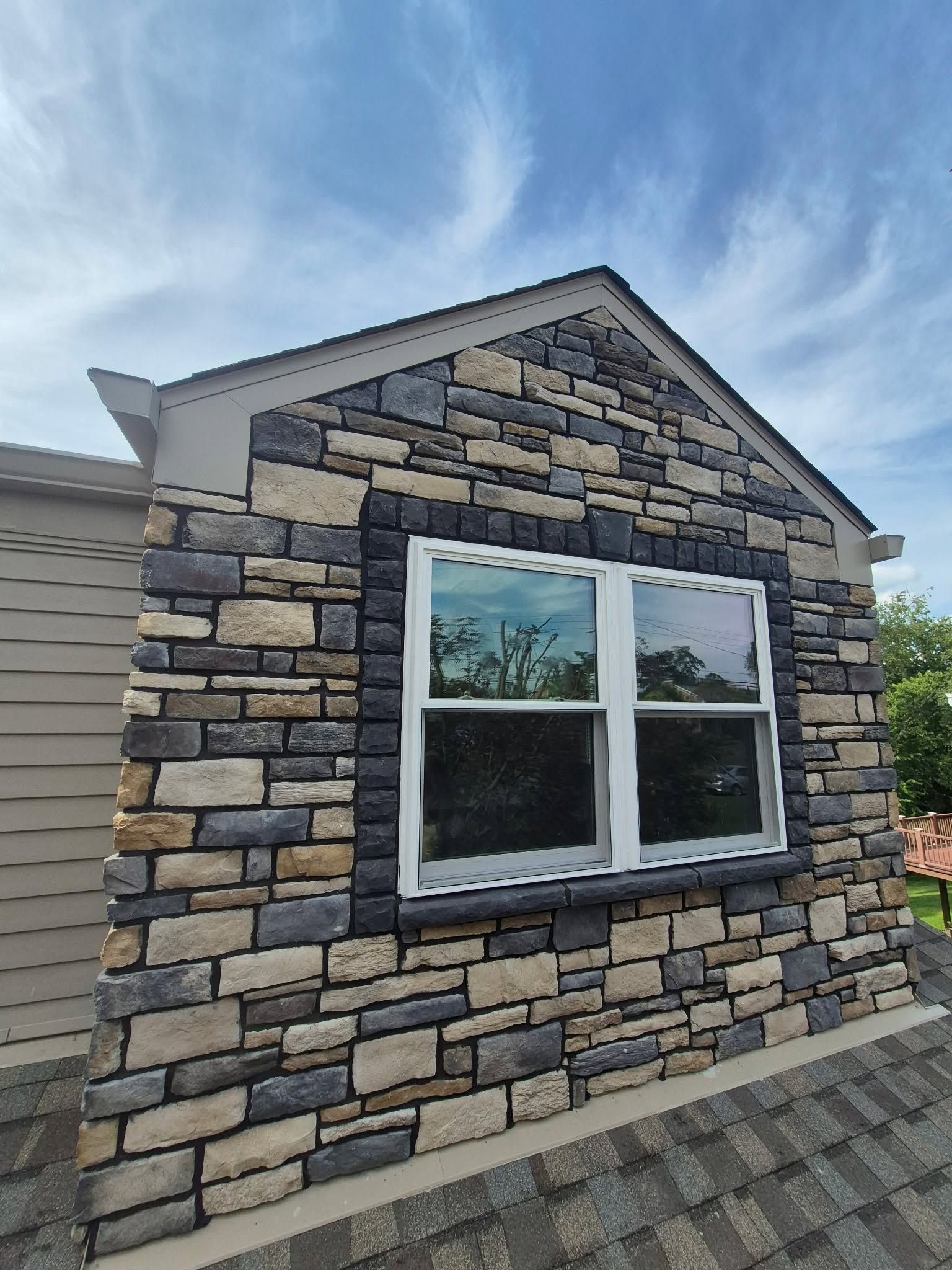 Stone-clad house exterior with a white-framed window and blue sky above