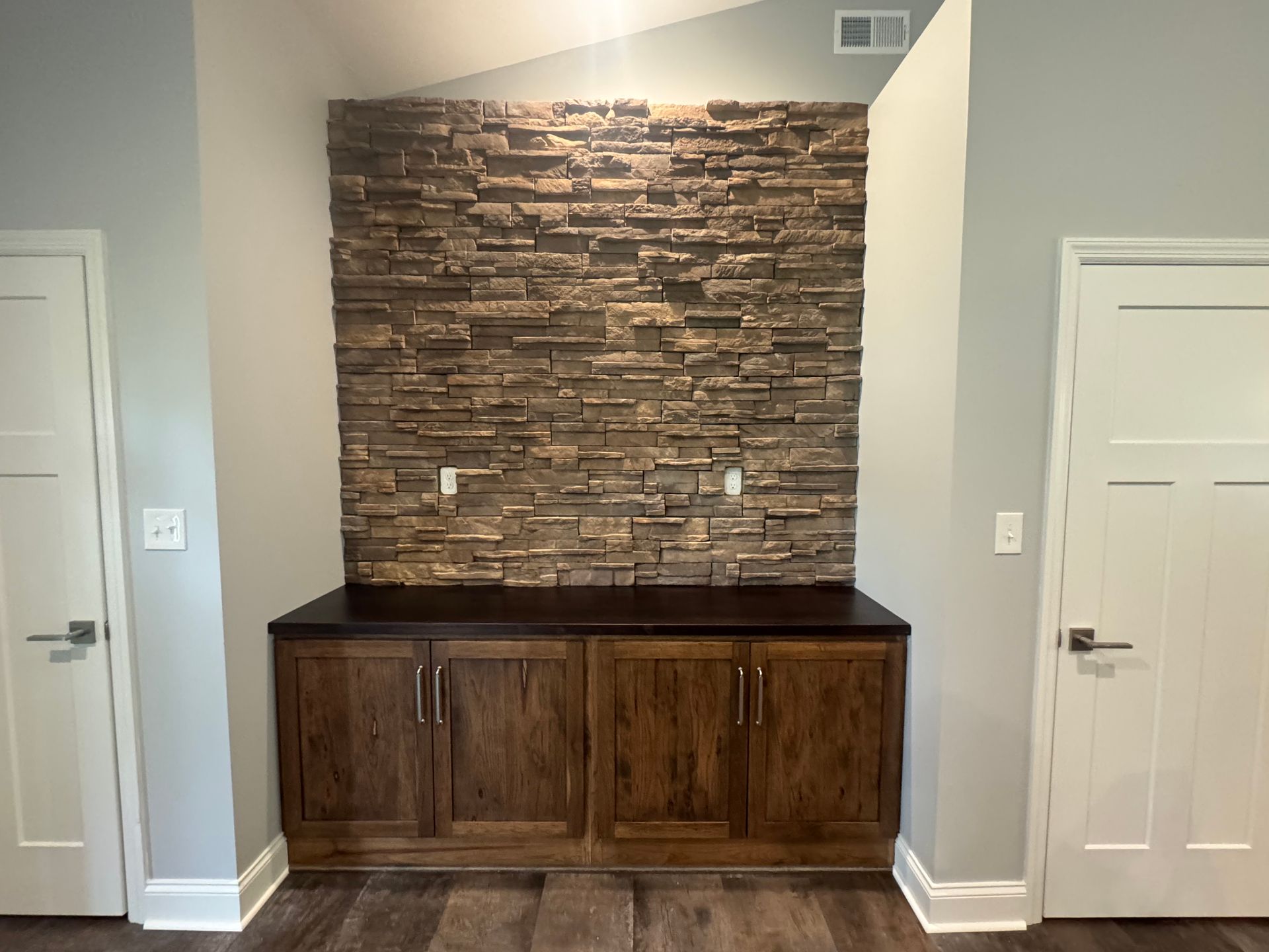 Hallway nook with a stone accent wall and dark wood cabinet between two white doors