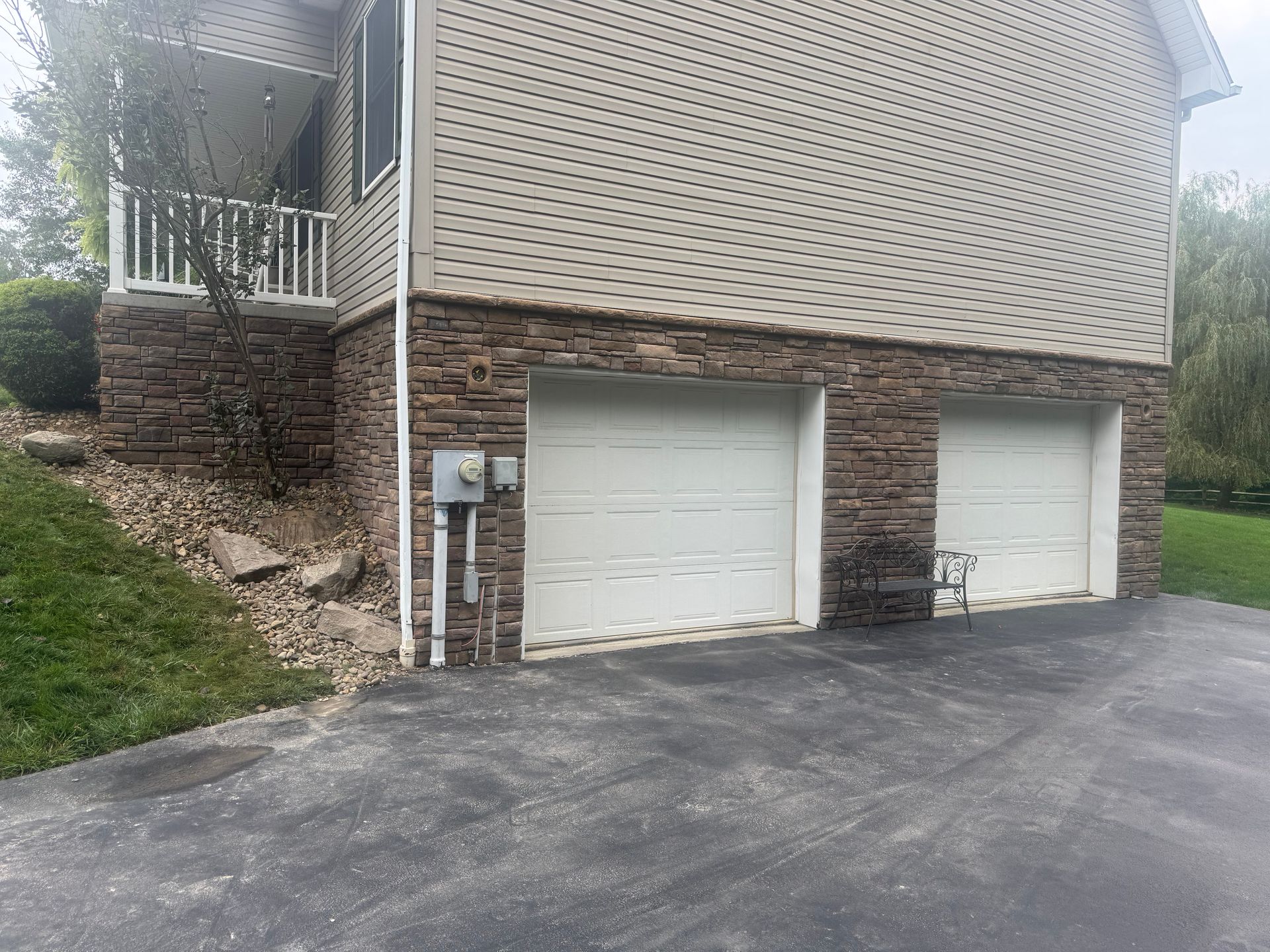 Two white garage doors on a house with stone siding and a sloped driveway.