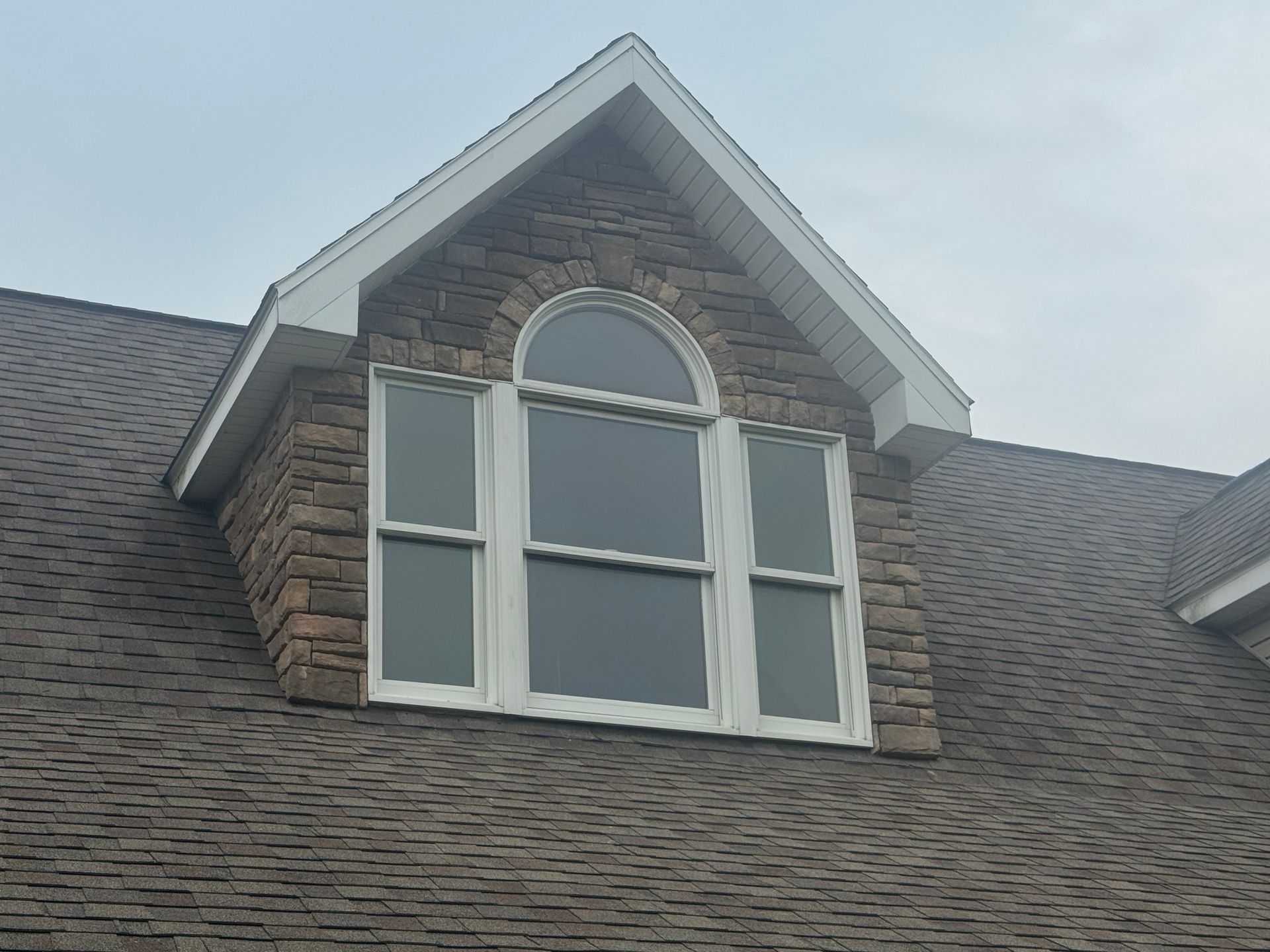 Dormer window with white trim and arched top on a gray shingled roof
