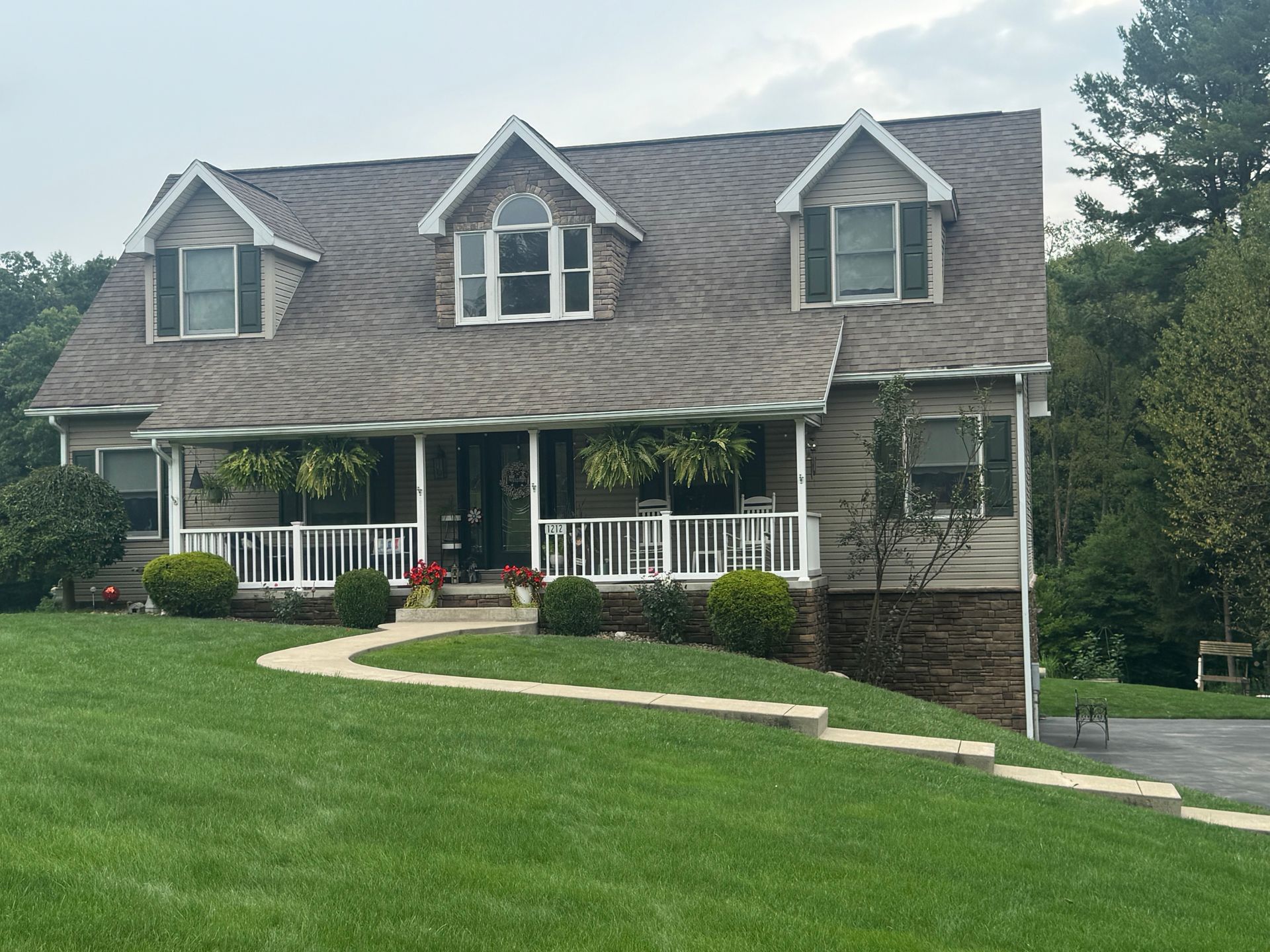 Two-story gray house with white porch railing and green lawn on a sloped yard