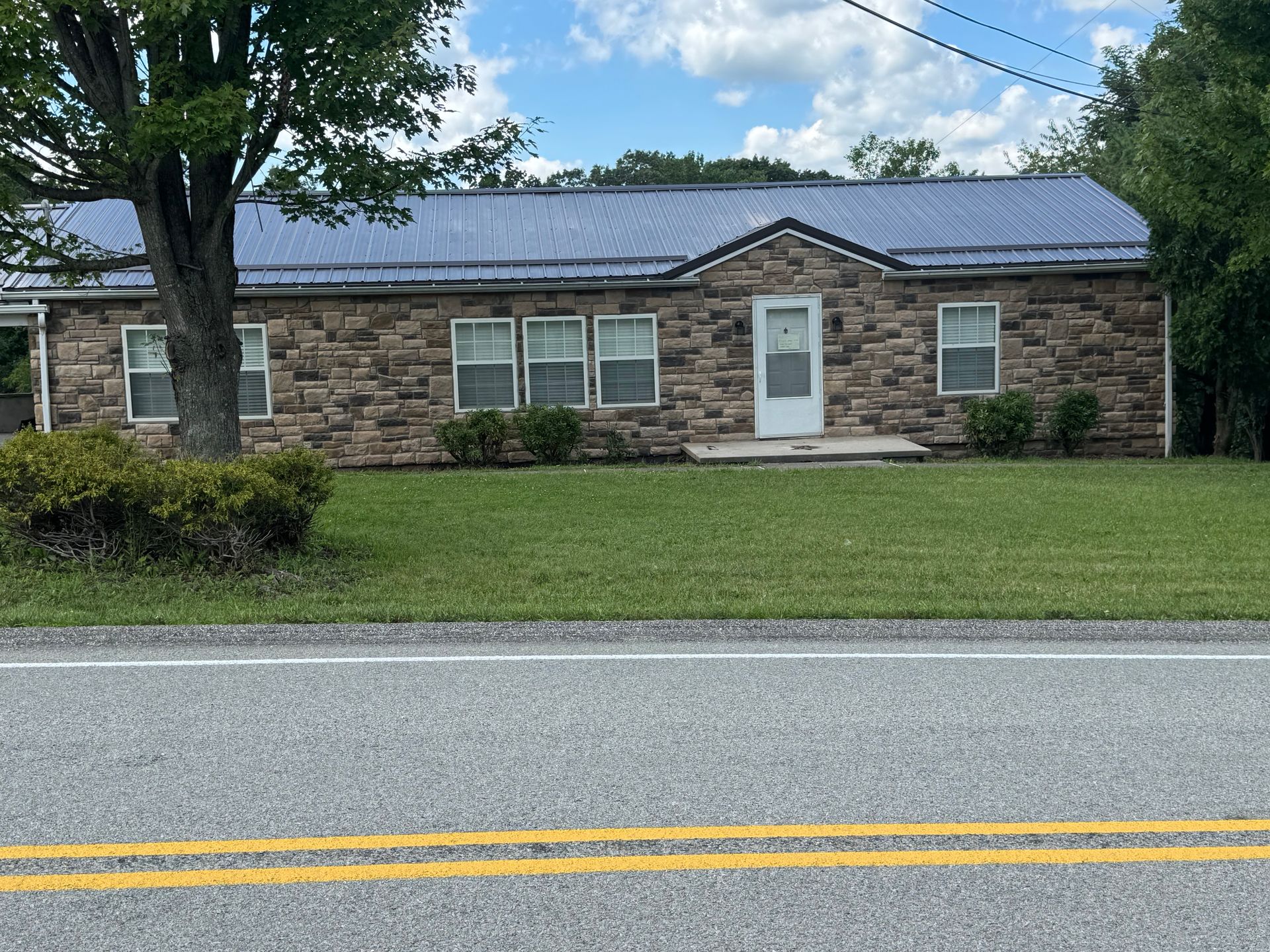 Single-story stone house with white door, front lawn, and road in the foreground