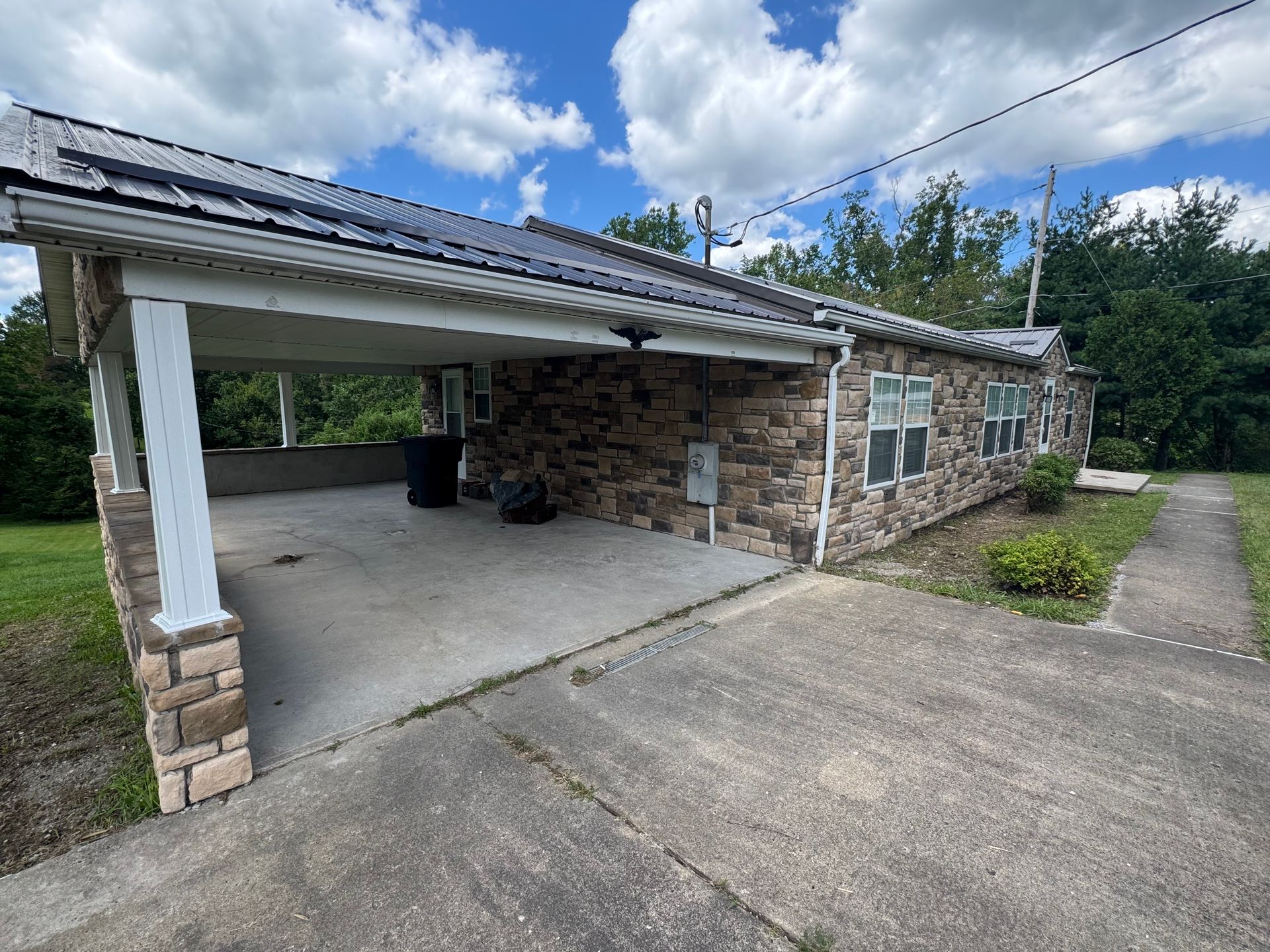 Stone house with a covered carport, solar panels on the roof, and a driveway beside it.