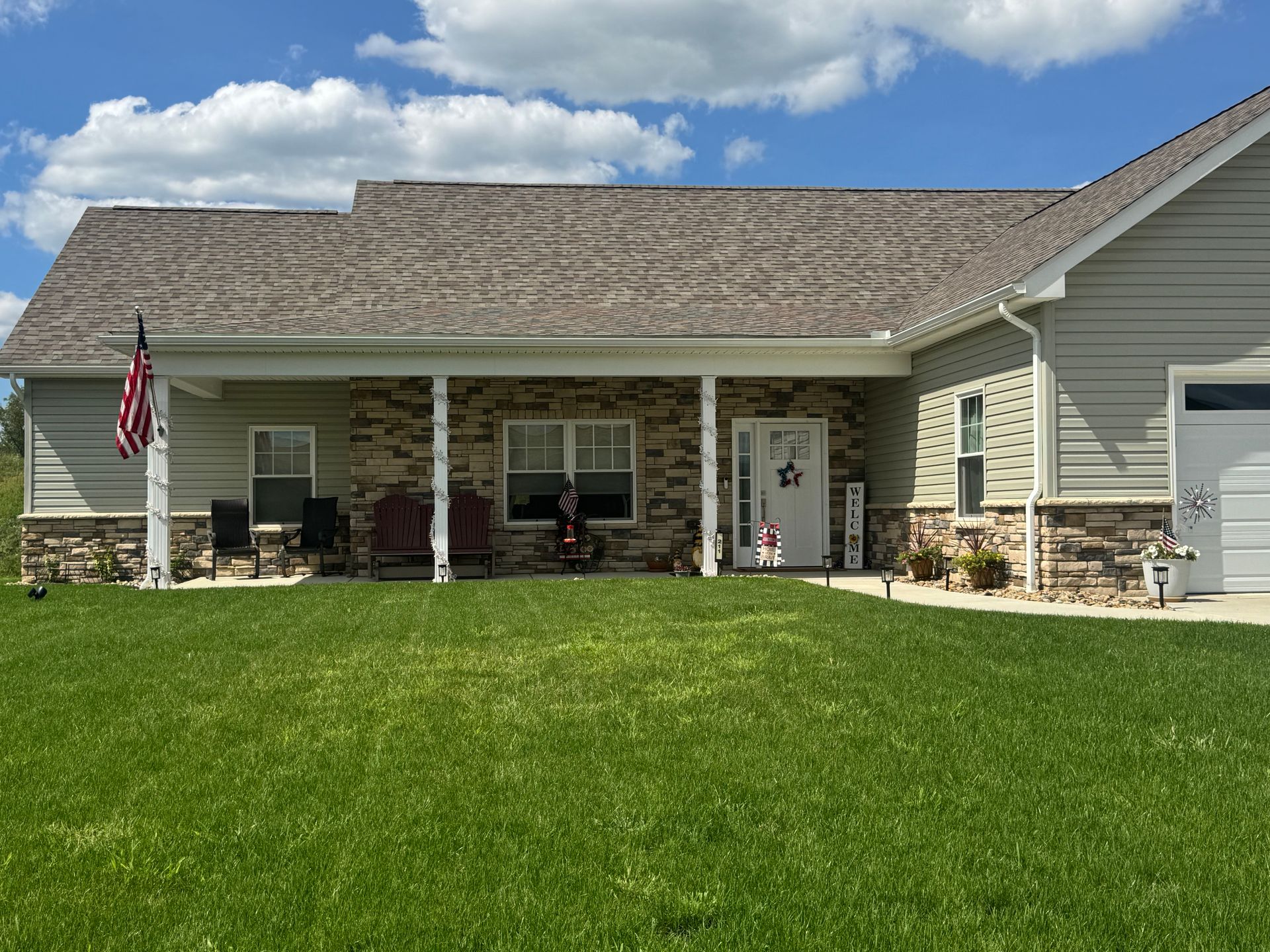 Suburban house with a covered front porch, American flag, and large green lawn under a blue sky