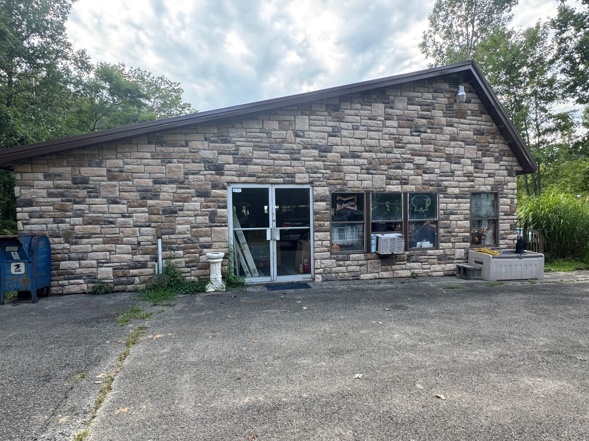 Stone-front commercial building with large windows and gravel parking lot under cloudy sky