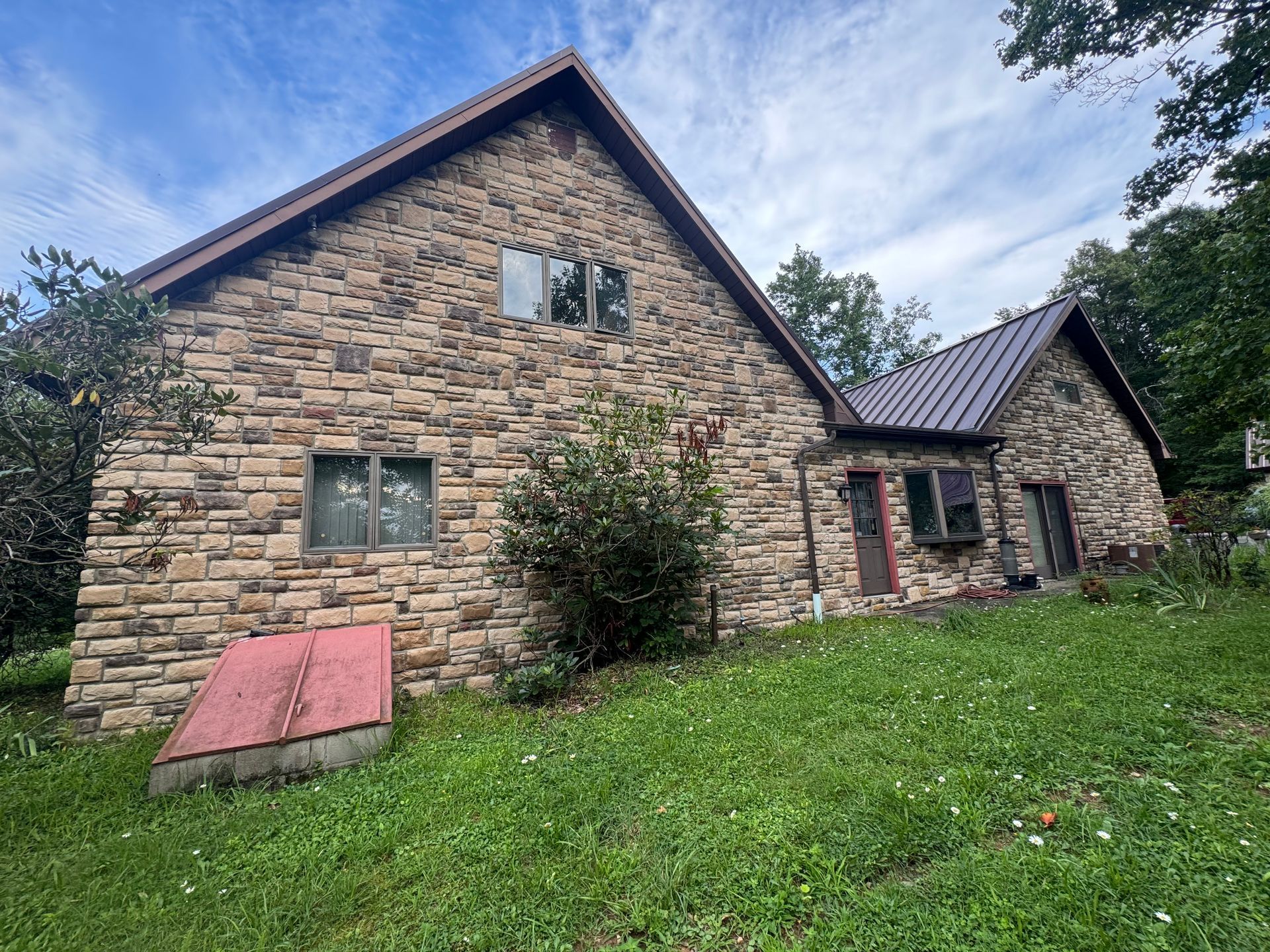 Stone house with a steep roof on a grassy hillside under a partly cloudy sky