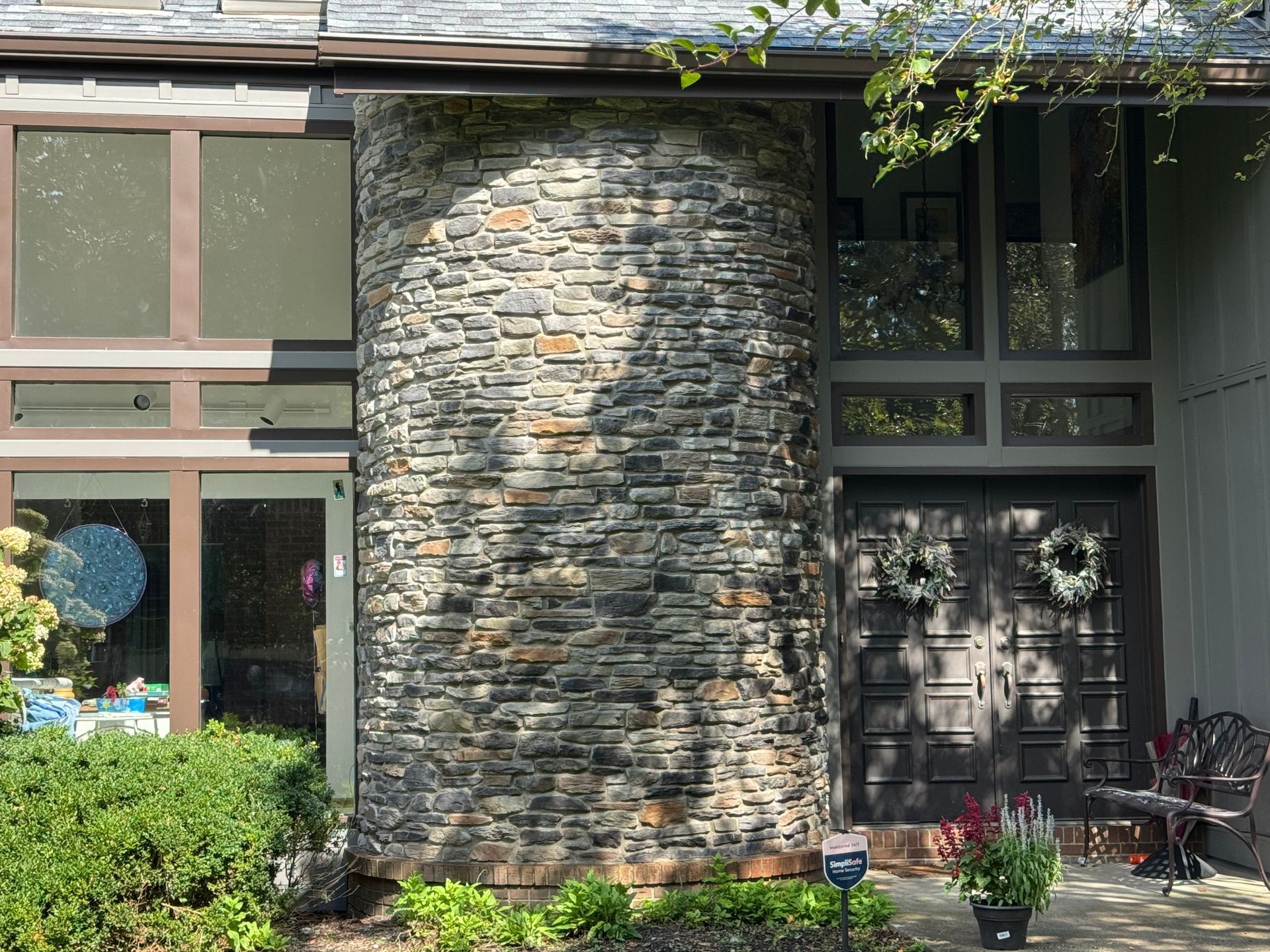 Stone-clad house entrance with glass windows, a dark front door, and potted plants by the steps