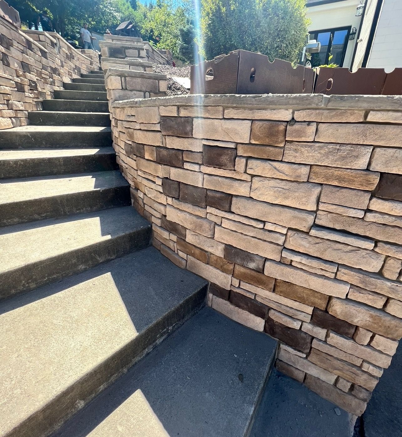 Stone retaining wall and concrete steps on a sunny outdoor staircase with landscaped steps.