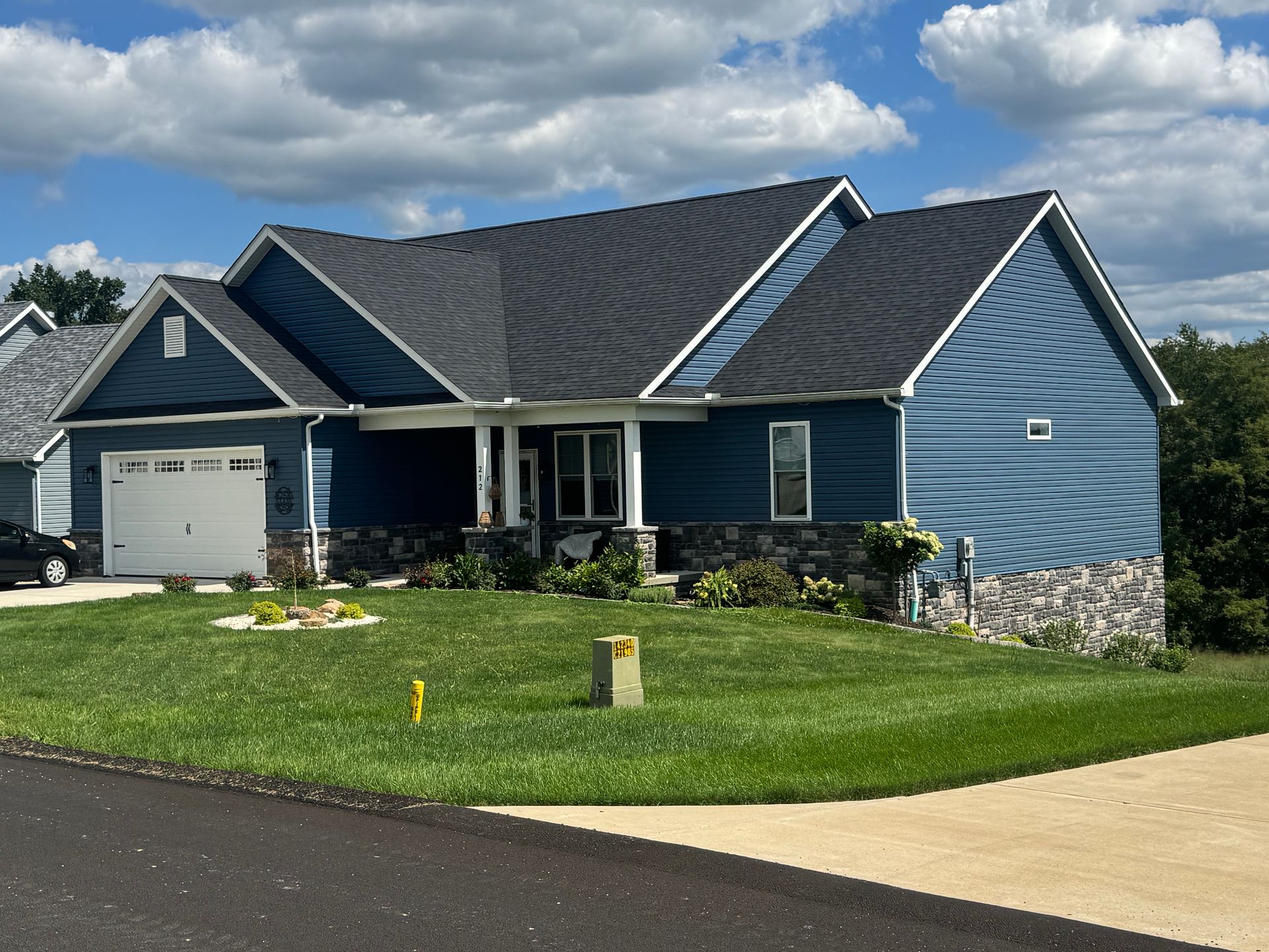 Blue single-story house with white trim, a garage, and a green lawn under a cloudy sky