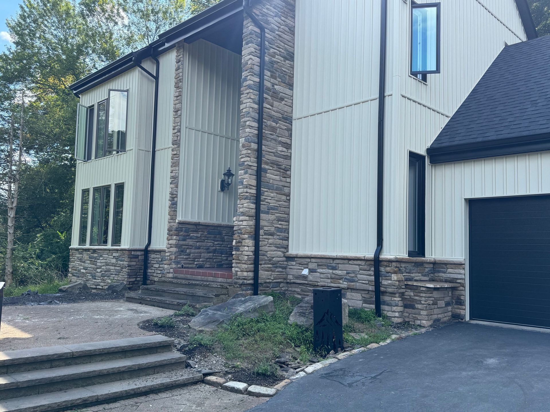 Modern two-story house with stone accents, front steps, and a dark garage door beside a driveway