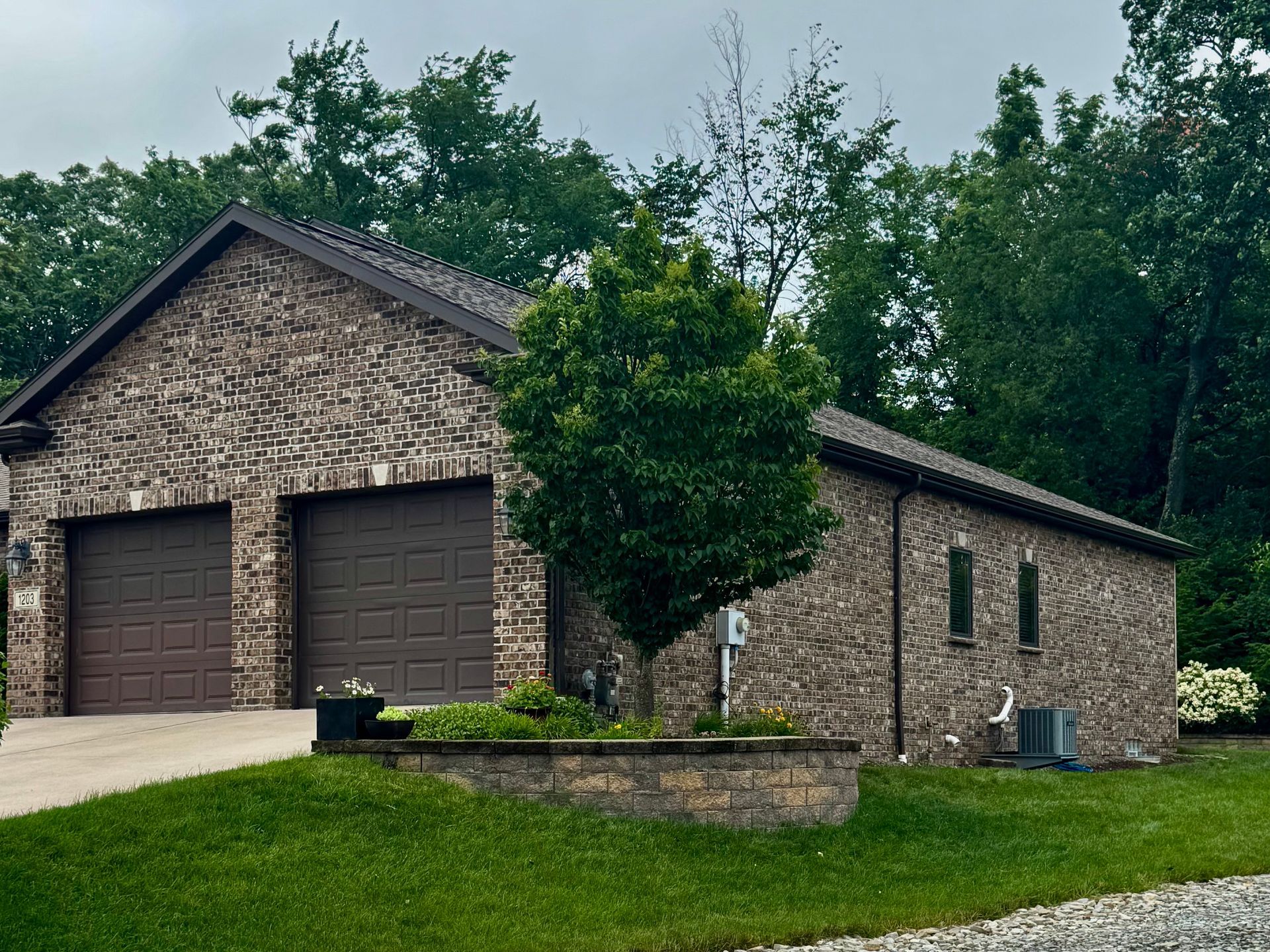 Two-car garage with stone exterior and brown doors, surrounded by trees and green lawn