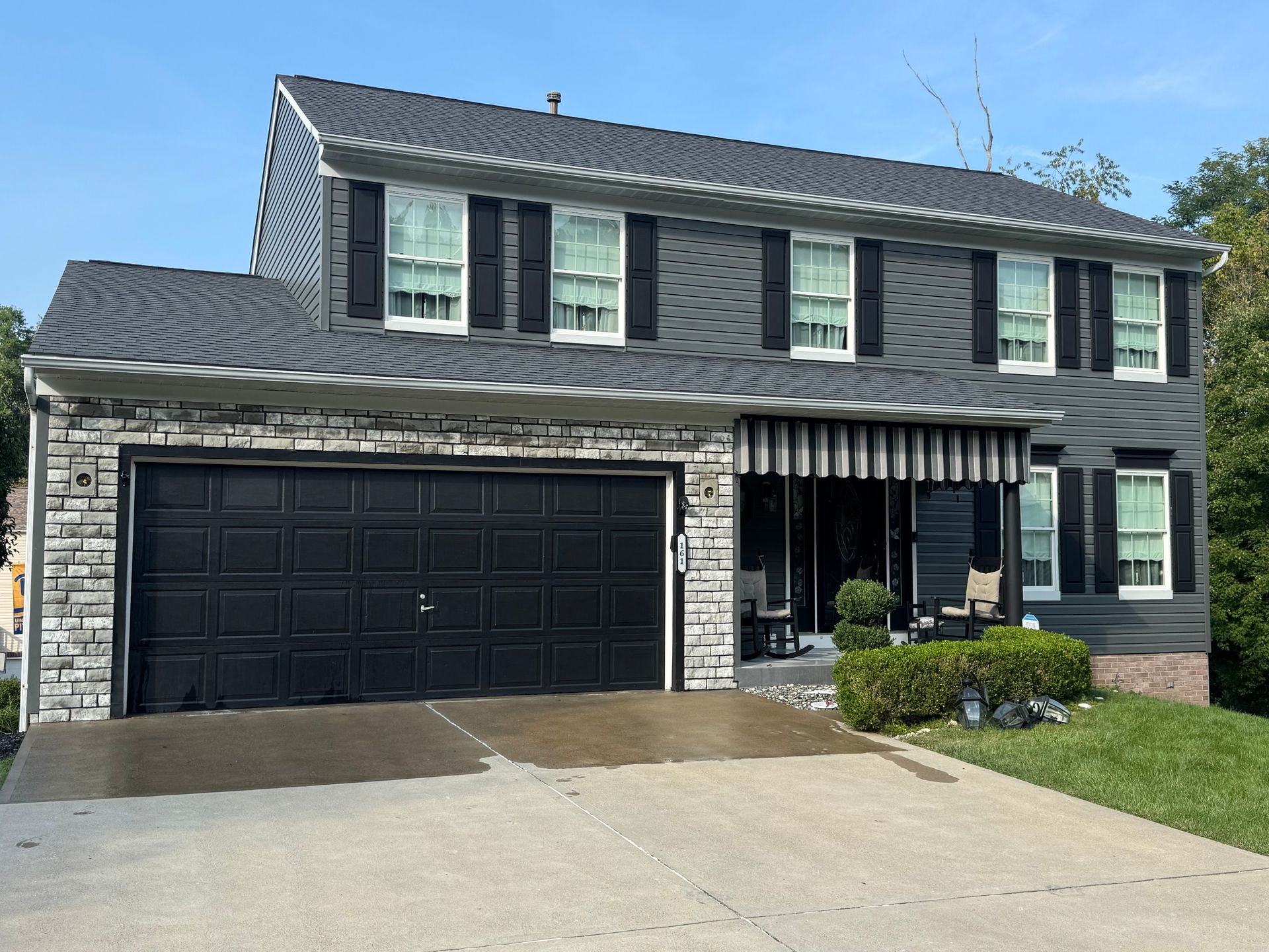 Two-story dark gray house with black garage, white trim, and a striped front awning by a driveway