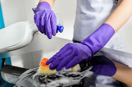 A person wearing purple rubber gloves is washing a pot with a sponge.