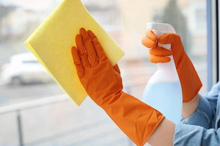 A person wearing orange gloves is cleaning a window with a cloth and spray bottle.