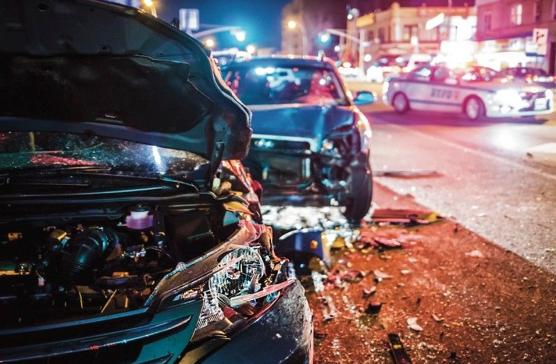 Cars wrecked in a night collision; police vehicle with flashing lights in the background.