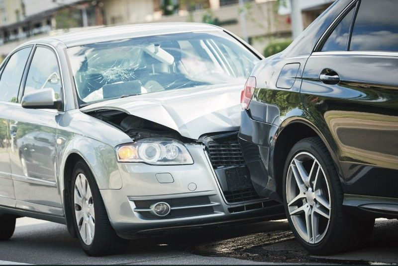 Silver car crashed into the rear of a black car; both vehicles damaged, likely a collision.