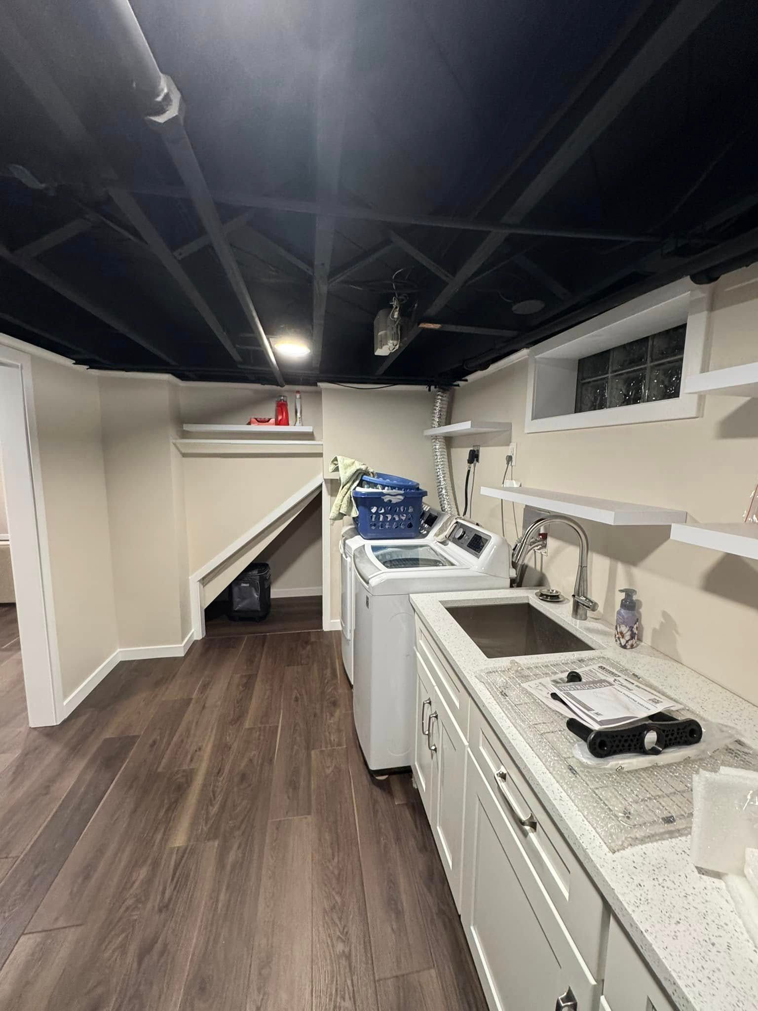 Long narrow basement kitchenette with white cabinets, dark wood floor, and laundry area at the far end