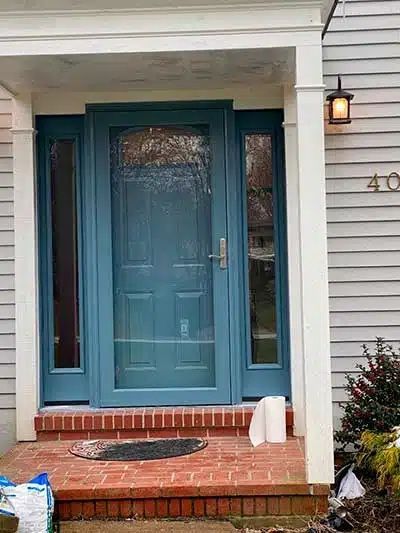 Blue front door with brick steps, white siding, and porch light at a house entrance