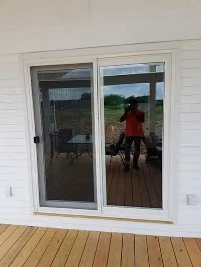 Person reflected in a sliding glass door on a wooden deck with white siding