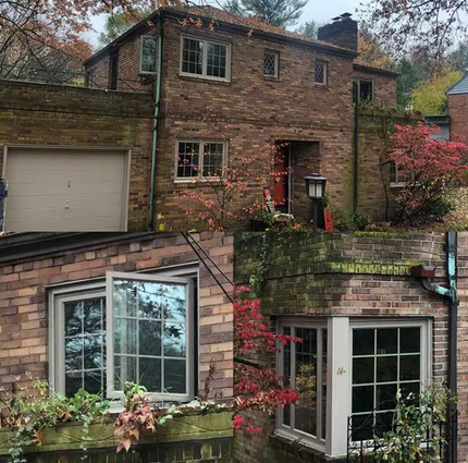Brick house facade with garage, windows, and red autumn foliage on a hillside.