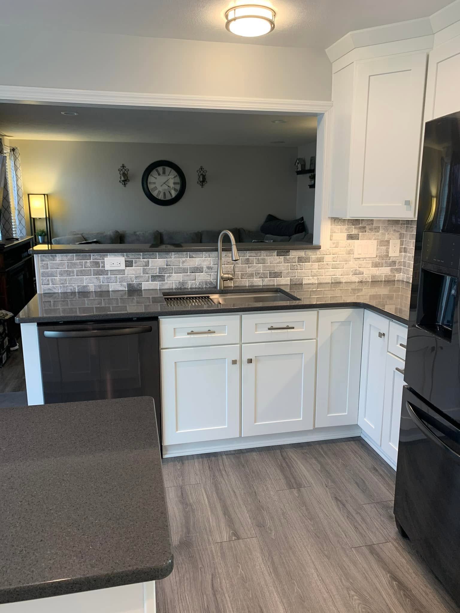 Compact kitchen with white cabinets, gray countertops, tile backsplash, and a black stove and sink.