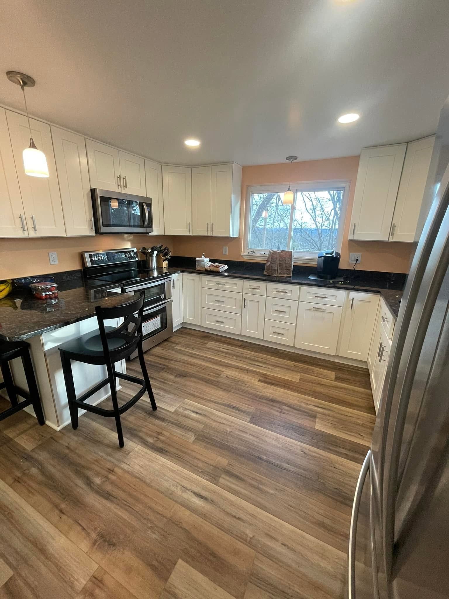 Bright kitchen with white cabinets, black countertops, wood floors, and stainless steel appliances.