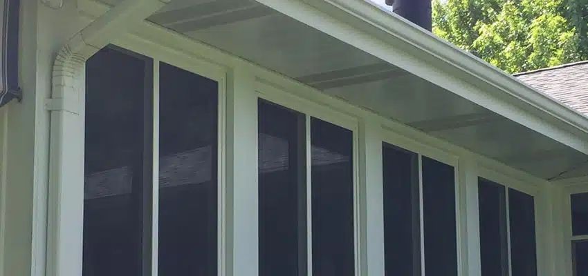 White-trimmed screened porch on a house with dark screen panels and green trees in the background