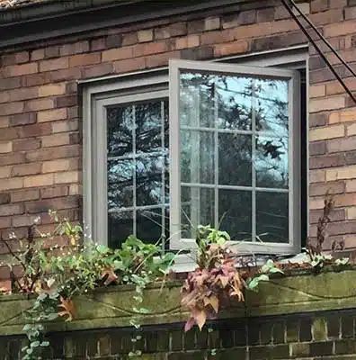 Brick house window with white trim, partially open, framed by climbing ivy and leaves on the sill