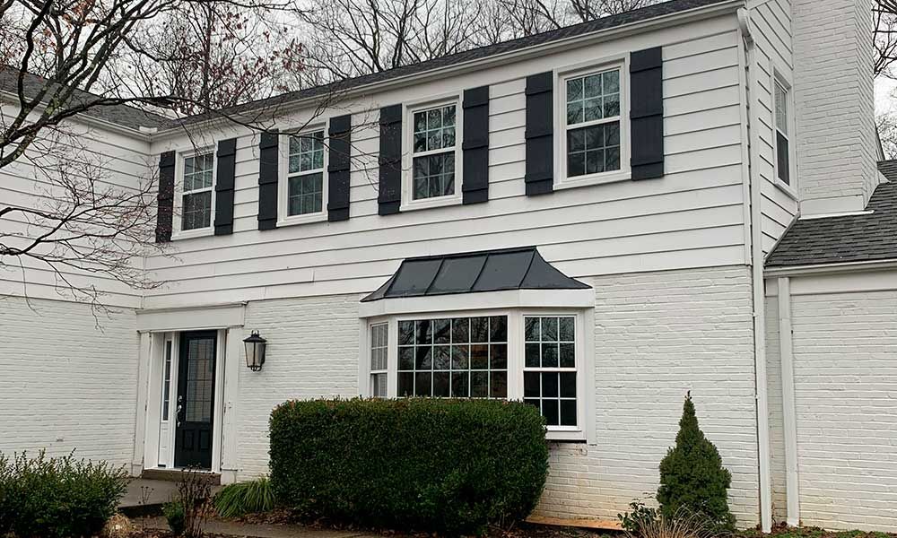White two-story house with black shutters and awning over the front windows