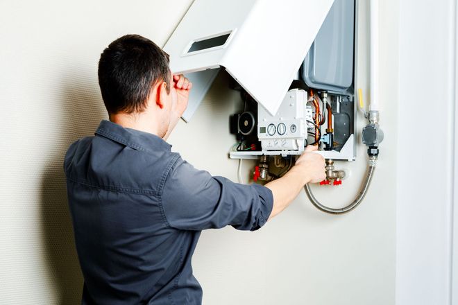 Technician inspecting an open wall-mounted boiler with tools in a home utility area