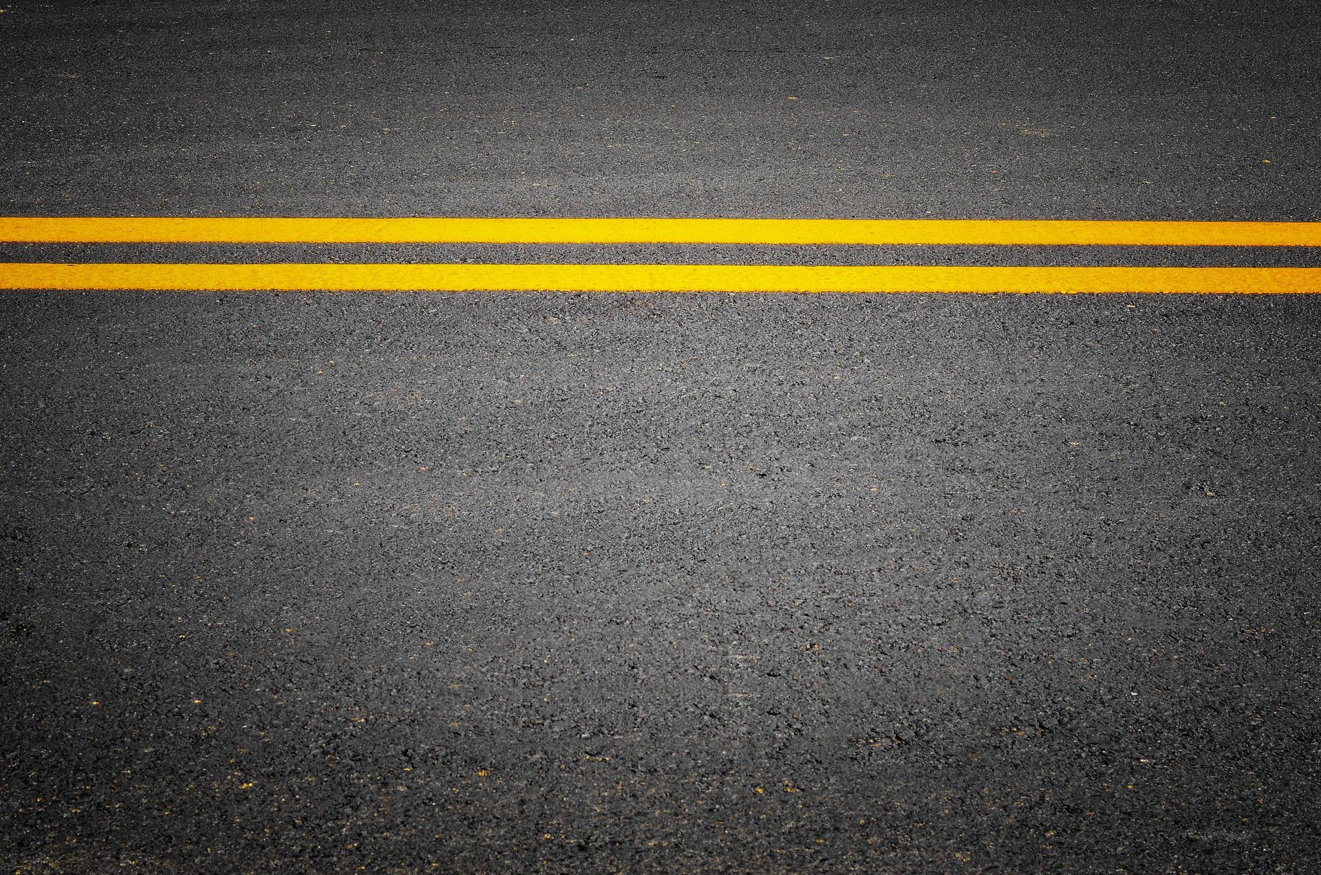 Double yellow lines painted on a black asphalt road.