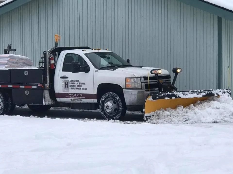 Snowplow truck plowing snow in front of a blue building on a snowy day.