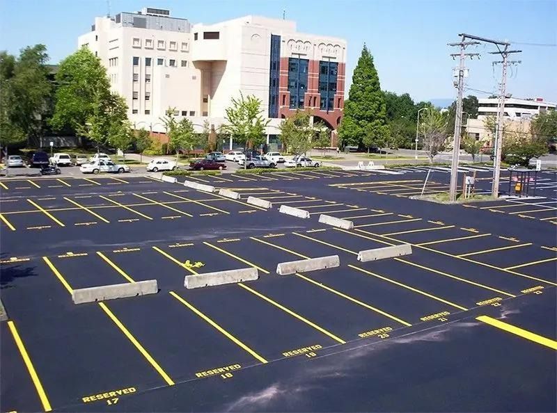 Parking lot with yellow painted lines and concrete barriers, building in background.