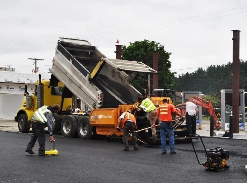Asphalt paving crew at work; dump truck unloading asphalt into a paving machine.
