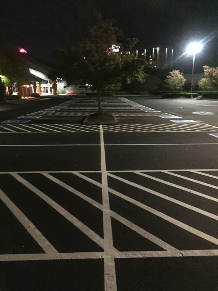 Empty parking lot at night with bright overhead lights and a tree in the center.