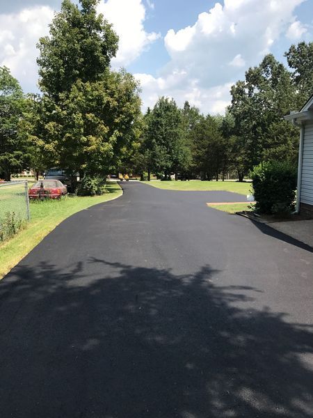 Black asphalt driveway curving towards trees on a sunny day.