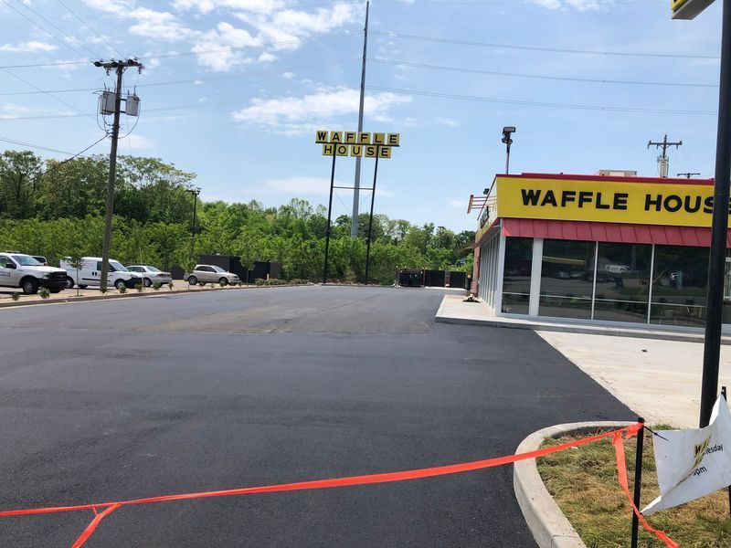 A newly paved parking lot in front of a Waffle House restaurant, with cars and a sign in the background.