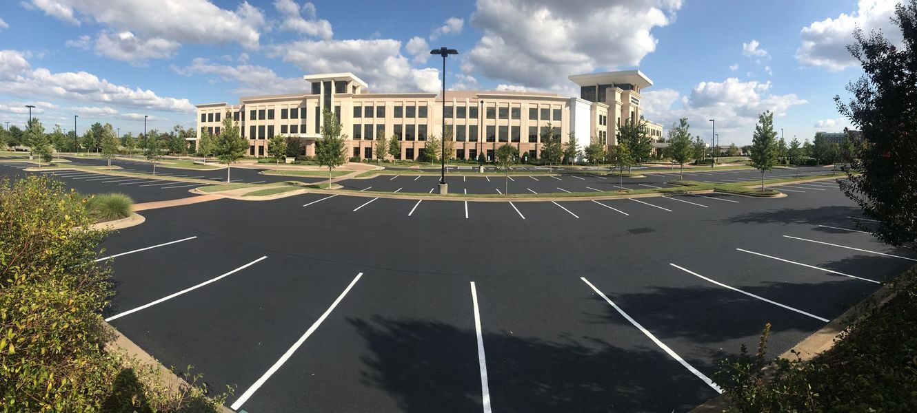 Wide shot of an empty parking lot in front of a large beige building under a partly cloudy sky.