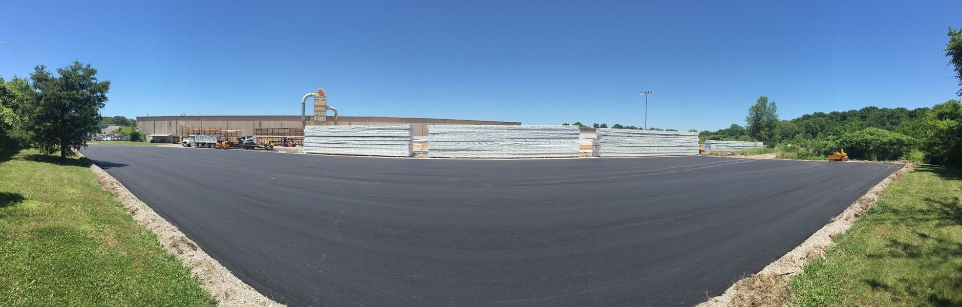 Wide view of a newly paved asphalt parking lot with a building in the background, under a clear blue sky.