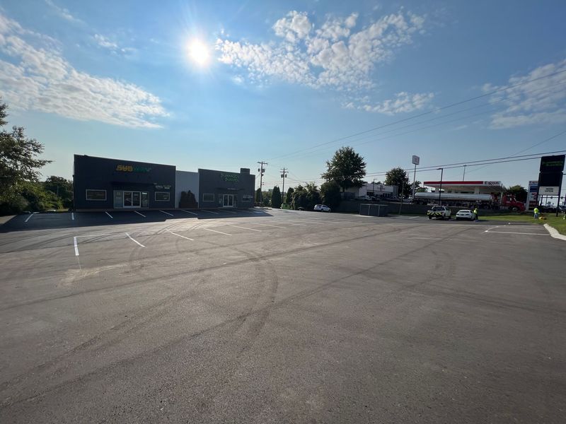 A mostly empty parking lot in front of a dark-colored building on a sunny day.